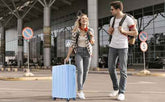 Two people with luggage walking outside an airport terminal.