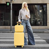 Woman with blonde hair holding coffee and pulling yellow ABS spinner luggage set with 14-inch carry-on and cosmetic case on city street