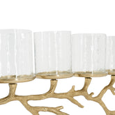 A close-up of a candle holder with clear textured glass candle sleeves mounted on a branch-like gold metal base, shown against a white background.