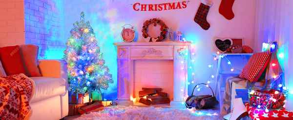 A cozy Christmas living room scene with a lit decorated tree, fireplace, stockings, and wrapped gifts under red &