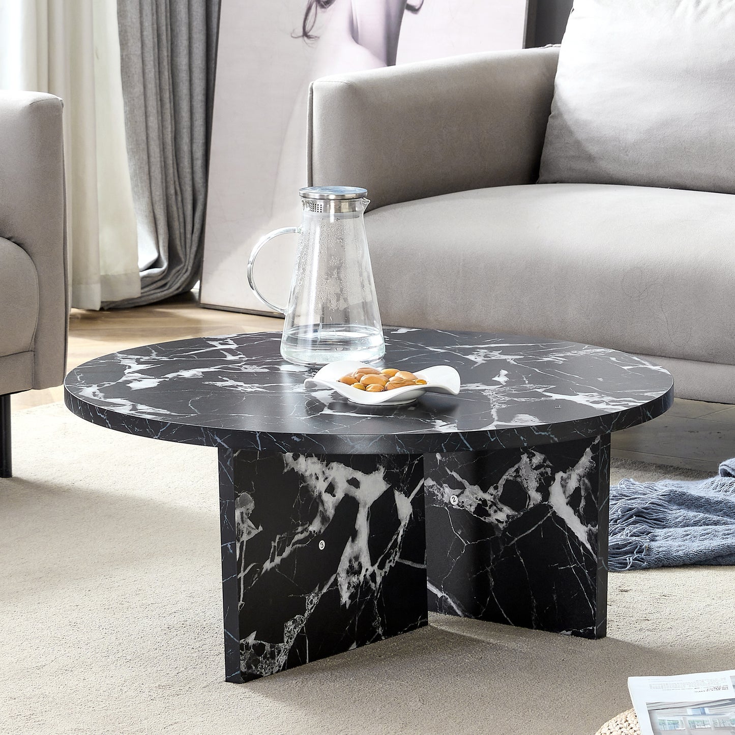 Modern minimalist black MDF round coffee table styled in a living room with faux marble surface and cross-leg base.