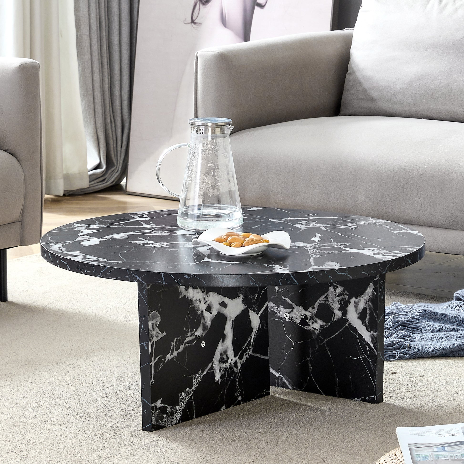 Modern minimalist black MDF round coffee table styled in a living room with faux marble surface and cross-leg base.