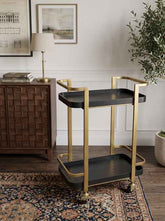 Stylish black and gold metal bar cart with two tiers, gold frame, black trays, and casters for easy movement in a modern living room