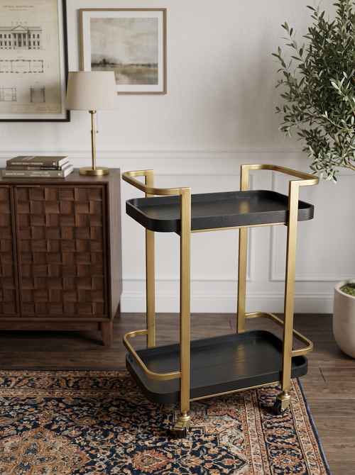 Stylish black and gold metal bar cart with two tiers, gold frame, black trays, and casters for easy movement in a modern living room