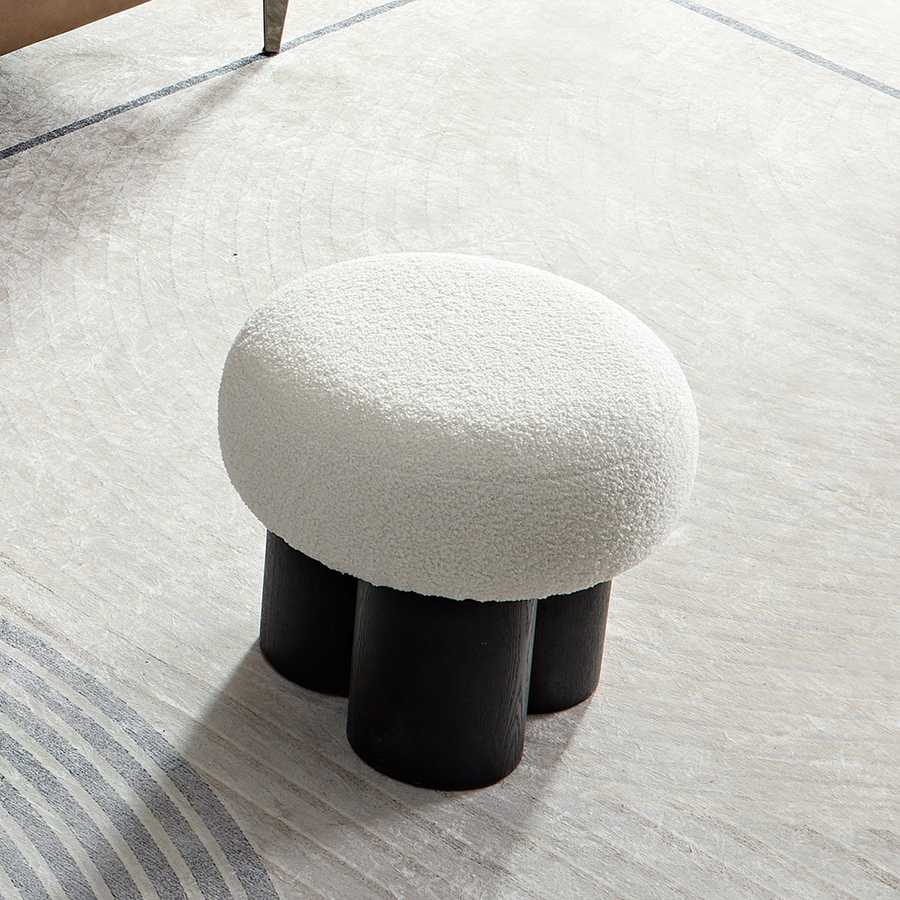Small round stool with white cushioned top and black cylindrical legs on a light wooden floor.