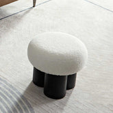 Small round stool with white cushioned top and black cylindrical legs on a light wooden floor.