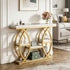 A modern console table with a white marble-look top and shelf surfaces, supported by a gold-tone metal frame with interlocking circular arches. The table is styled in a bright living room with decorative items, a floral arrangement, and a sofa in the background.