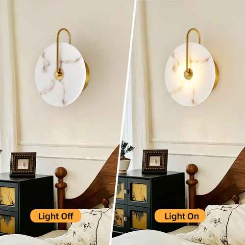 A split comparison of a modern wall sconce in a bedroom, showing the light off on the left and on the right. The sconce features a round white marble-look shade with gold trim and a curved gold metal arm.