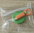 Green and orange plastic tool on a wooden surface with clear plastic wrap.