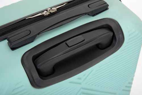 Close-up of a hard-shell suitcase in mint green with black telescoping handle and zipper pull.