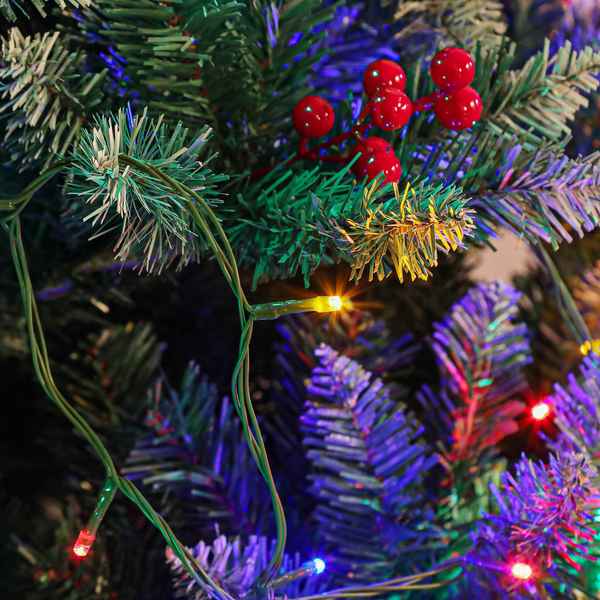 Close-up of multicolor LED fairy lights on a green artificial pine tree branch, with red berries visible in the background.