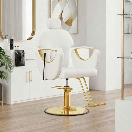 A modern salon barber chair with a white upholstered seat and gold metal armrests, backrest details, and a gold hydraulic base, shown in a bright, contemporary salon interior.