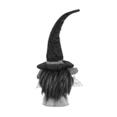 A black witch-themed decorative gnome head with a tall curved pointed hat, black faux hair, a checkered band, and small white wings, shown on a white background.