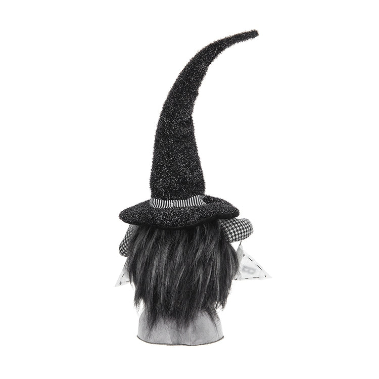A black witch-themed decorative gnome head with a tall curved pointed hat, black faux hair, a checkered band, and small white wings, shown on a white background.