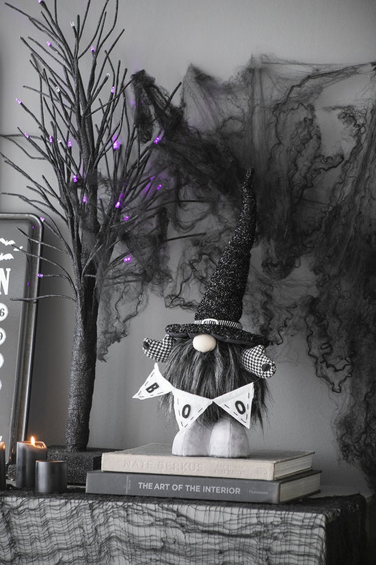 Decorative Halloween gnome with a banner on books, surrounded by Halloween decorations.