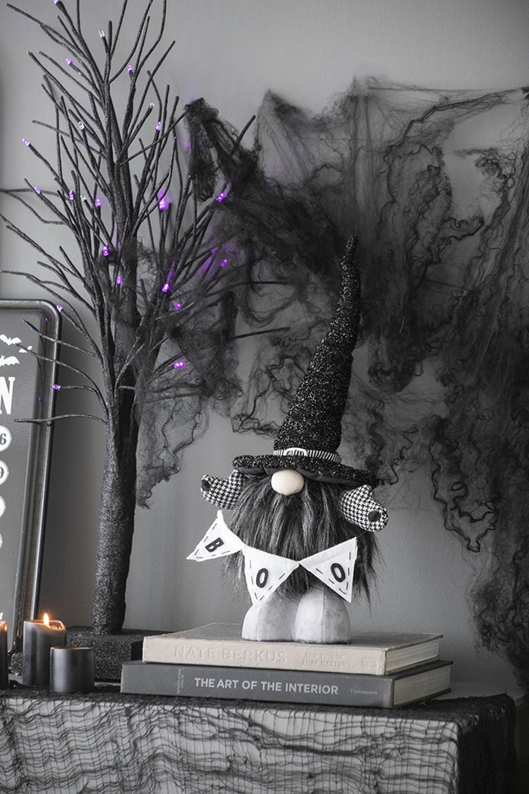 Decorative Halloween gnome with a banner on books, surrounded by Halloween decorations.