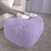Person sitting on a fluffy purple ottoman in a living room.