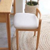 Wooden chair with white cushion next to a wooden table on a textured rug.