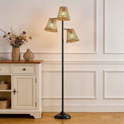 A three-light floor lamp with a black metal pole and three woven natural-fiber shades, shown lit in a styled room next to a wooden cabinet.