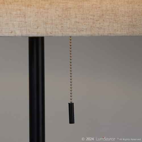 Close-up of a table lamp with a beige woven fabric shade, a black metal stem, and a black pull chain with a black weighted end, shown against a neutral gray background.