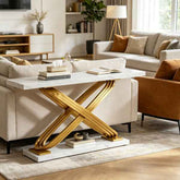 A modern console table in a styled living room, featuring a white marble top and a sculptural, interlocking gold metal base on a matching marble plinth.