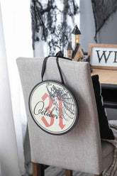 Halloween circle sign with spiderweb design and October 31 date, hanging on a chair with black ribbon, in festive home decor setting