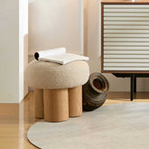 Round beige ottoman with wooden legs in a room setting.
