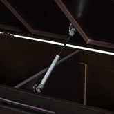 A close-up of a dark brown wooden storage cabinet with its lid open, supported by a silver metal hydraulic gas lift rod.