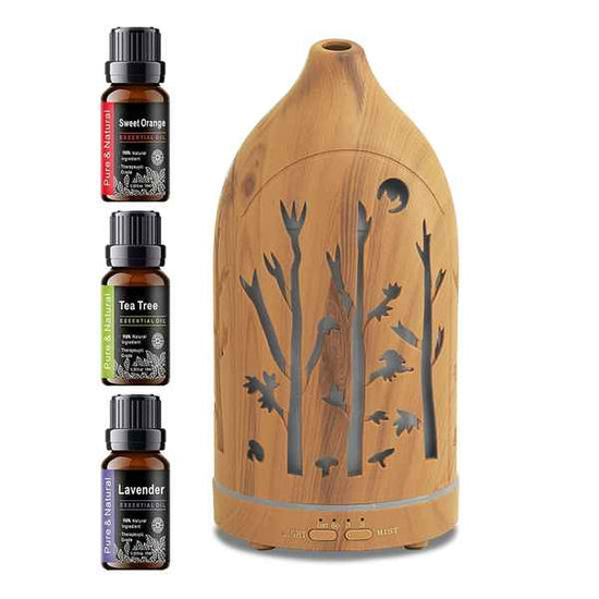 A bamboo diffuser with a tree silhouette cutout design, shown alongside three small essential oil bottles labeled Sweet Orange, Tea Tree, and Lavender on a white background.
