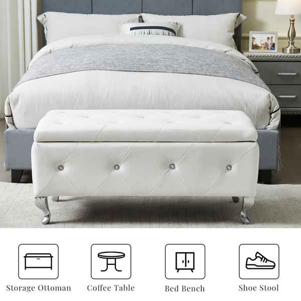 White tufted storage ottoman in front of a bed with gray bedding.