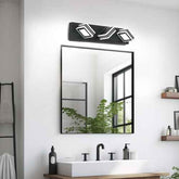 A modern black wall-mounted light fixture with three angled rectangular bulbs is installed above a rectangular mirror in a bright bathroom. The mirror reflects a window and greenery, and the sink and faucet are visible below.