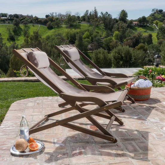 Two wooden lounge chairs on a patio with a scenic view of greenery.