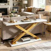 A modern console table with a white marble-look top and base, supported by a bold gold X-shaped metal frame, styled in a contemporary living room setting.