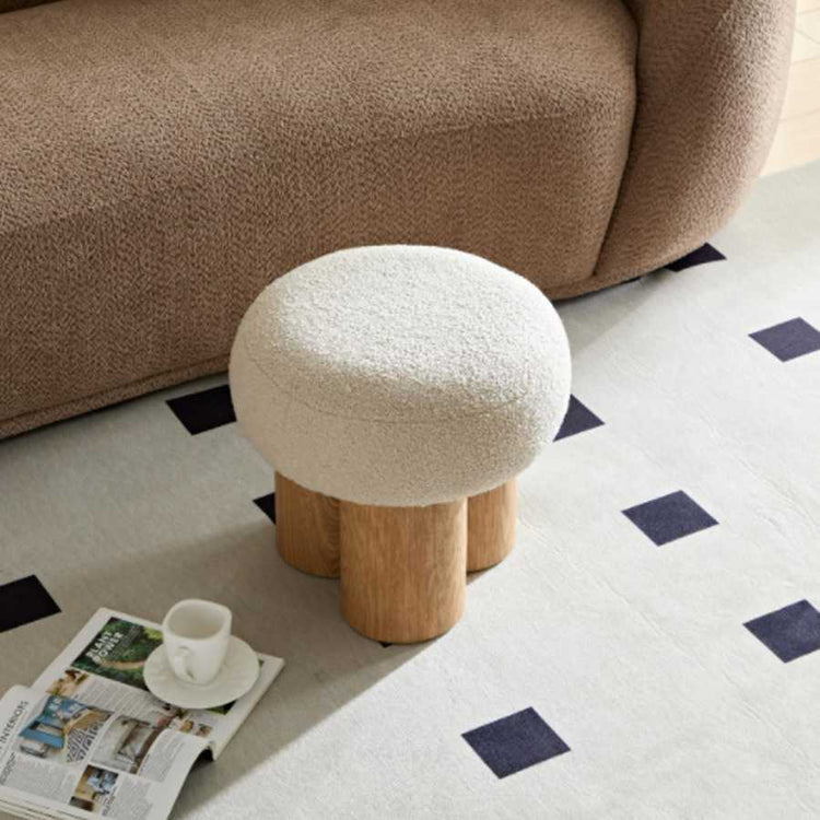 Round ottoman with wooden legs on a patterned rug next to a brown sofa.