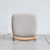 Gray cushioned chair with wooden base on a light gray floor and white wall background