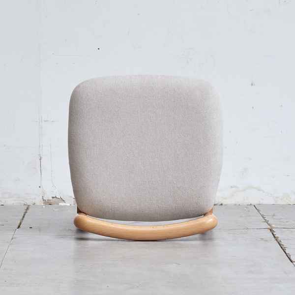 Gray cushioned chair with wooden base on a light gray floor and white wall background