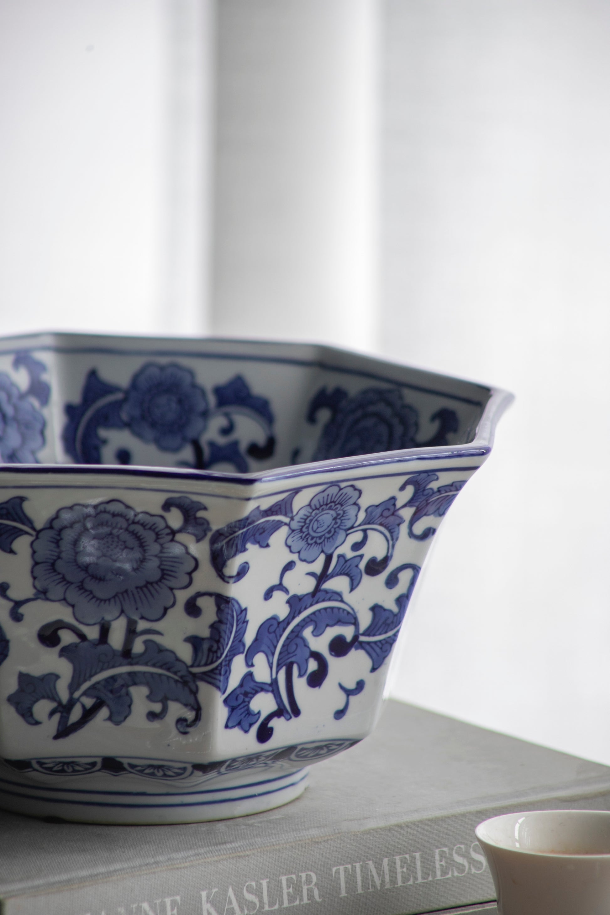 Side view of Blue and White Decorative Bowl - Porcelain, Elegant Design showing floral detailing and curved rim on a book stack.