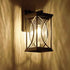 A rectangular outdoor wall sconce with a dark metal frame and textured clear glass panels, mounted on a wall and casting a warm yellow light.