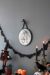 Halloween circle sign with spiderweb and October 31, hanging on a gray wall with black bat garland and spooky decorations