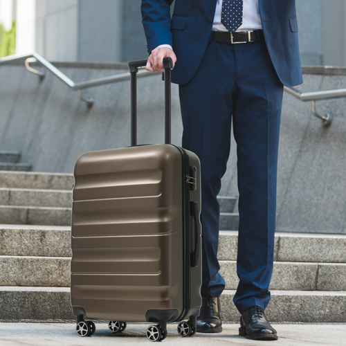 Businessman pulling brown 24-inch hardshell suitcase with telescoping handle, four spinner wheels, on airport stairs for travel