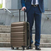 Businessman pulling brown 24-inch hardshell suitcase with telescoping handle, four spinner wheels, on airport stairs for travel