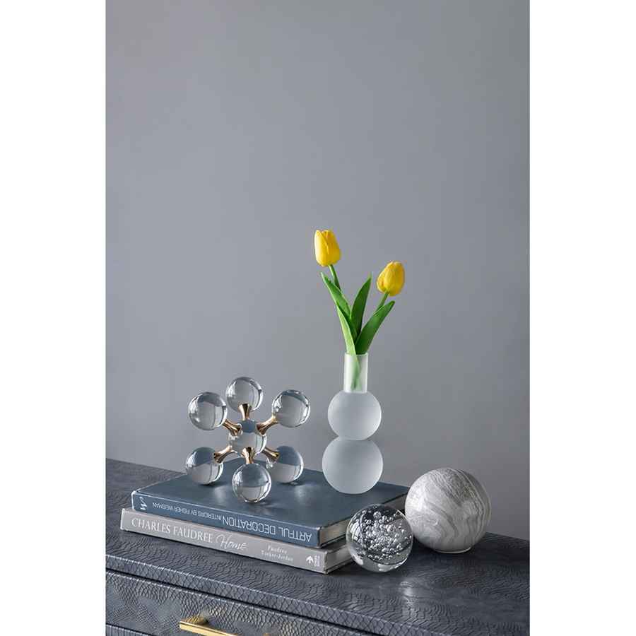 Decorative objects including a vase with yellow tulips, books, and crystal sculptures on a gray surface.