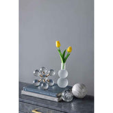 Decorative objects including a vase with yellow tulips, books, and crystal sculptures on a gray surface.