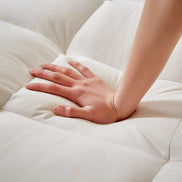 Hand pressing into soft tufted cushion of convertible beige velvet sofa bed with USB port. Highlights plush comfort and quality fabric.