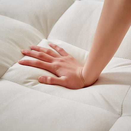 Hand pressing into soft tufted cushion of convertible beige velvet sofa bed with USB port. Highlights plush comfort and quality fabric.