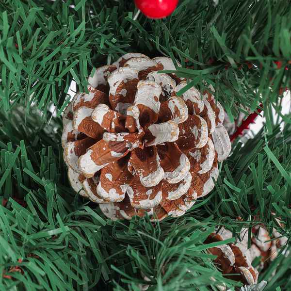 A decorative pinecone ornament with brown and white weathered detailing, nestled among green artificial pine needles with a red ornament partially visible at the top.
