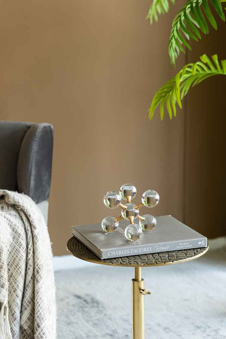 Decorative glass sculpture on a small table with a book underneath, against a neutral wall.