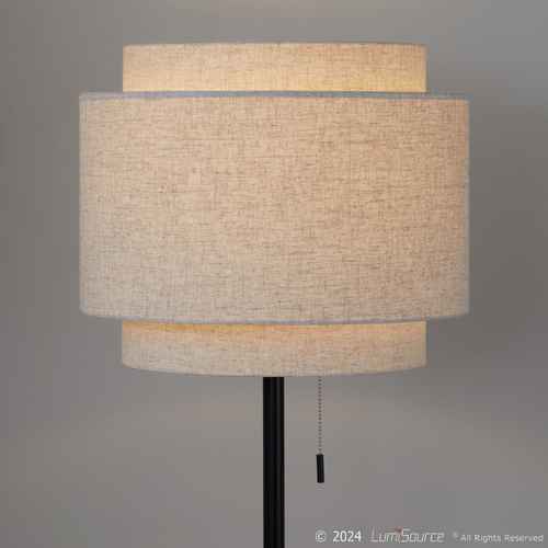 A modern floor lamp with a black metal stand and three horizontal drum shades made of textured beige linen, shown against a neutral gray background. A pull chain is visible at the bottom.
