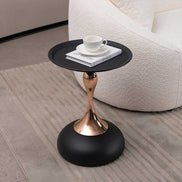 Modern Metal Mermaid Tail Coffee Table with black round top and gold sculptural base beside a white boucle sofa. Stylish metal accent table.