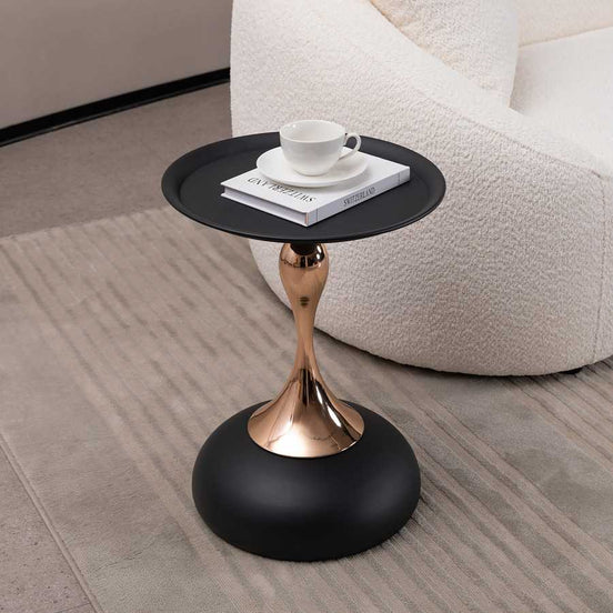 Modern Metal Mermaid Tail Coffee Table with black round top and gold sculptural base beside a white boucle sofa. Stylish metal accent table.